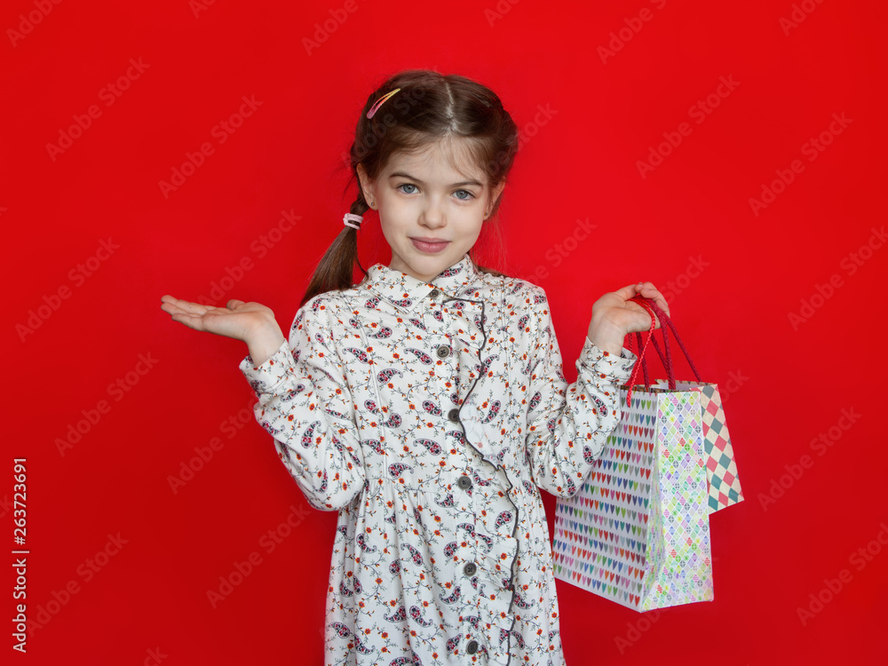 smiling young girl holding a gift bags in her hands on a red background, concept of advertising, sales, discounts smiling young girl holding a gift bags in her hands on a red background, concept of advertising, sales, discounts