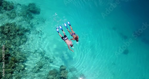 Aerial view around a young couple snorkeling above coral reef reaching deeper parts of the crystal clear water, Maldives. photo