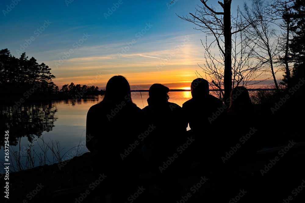 family of four looking at the sunset over a lake
