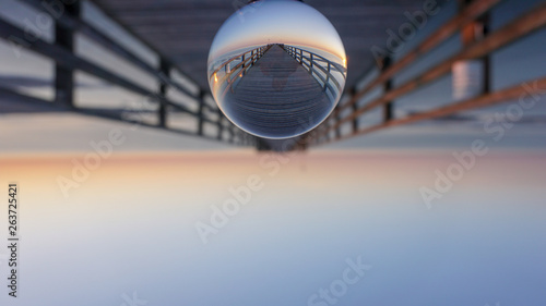 Fototapeta Naklejka Na Ścianę i Meble -  Seebrücke am Ostsee-Strand von Prerow auf dem Darß im Sonnenaufgang in Glaskugel - Lensball  Wallpaper