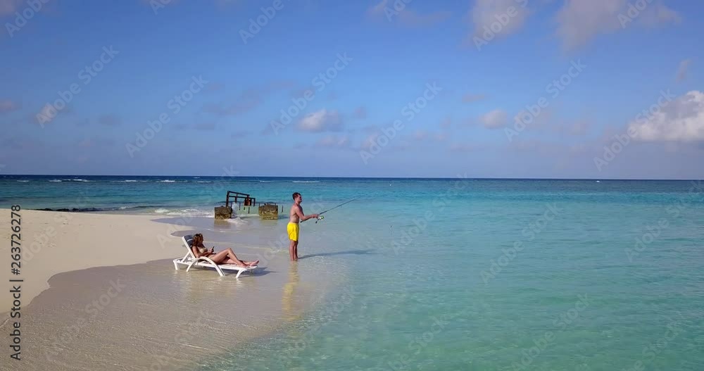 Tropical island, woman looking at phone using social media while man fishes in beautiful nature Tropical island, woman looking at phone using social media while man fishes in beautiful nature