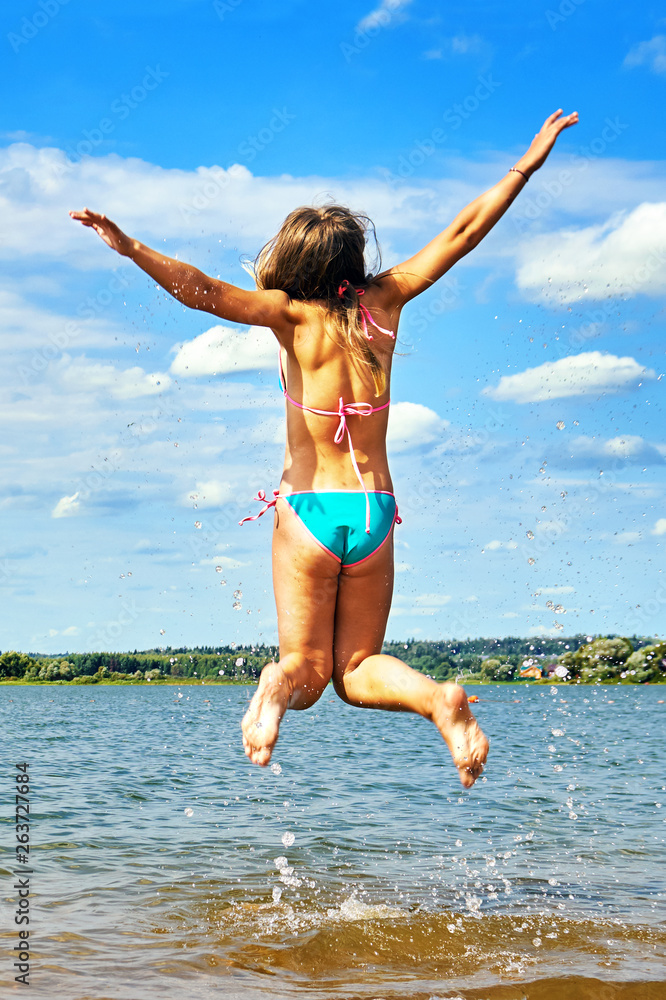 Teenager girl wearing bikini with spreading hands jumps high above the water  of a beautiful lake enjoying warm weather at summer vacations. Happy summer  vacations. Stock Photo | Adobe Stock