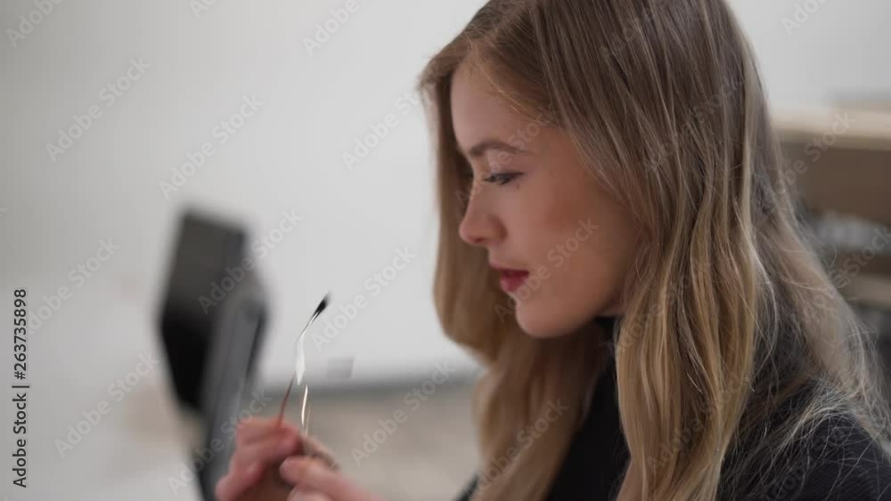 Close up of woman putting on glasses sat at her desk in office Close up of woman putting on glasses sat at her desk in office