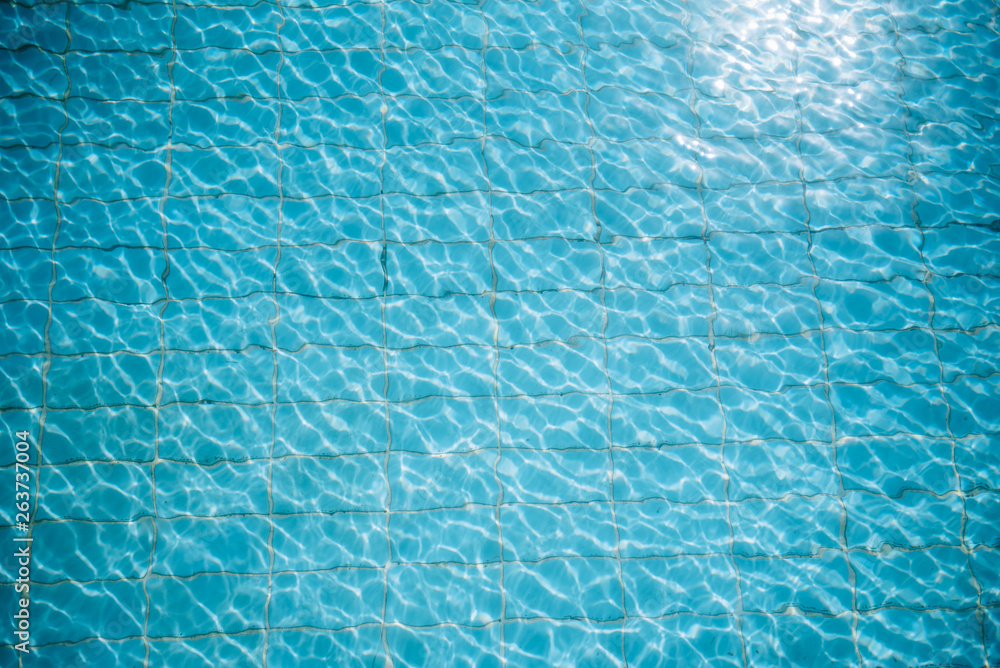 Water ripples on blue tiled swimming pool background. View from above.