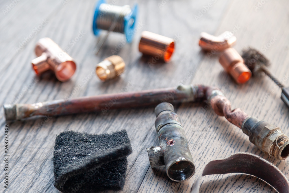 Close-up soldering, plumbing, construction professional tools, parts of copper pipes on a wooden background. Concept of professional repair of water supply, replacement old pipes with new ones Close-up soldering, plumbing, construction professional tools, parts of copper pipes on a wooden background. Concept of professional repair of water supply, replacement old pipes with new ones