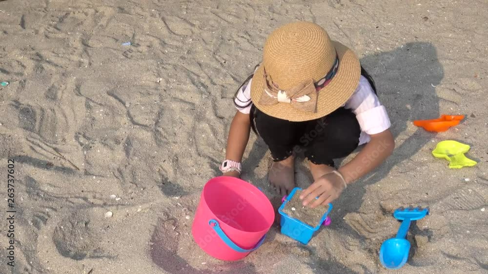 Asian child girls wearing hats, playing sand piles on the beach on family holidays Asian child girls wearing hats, playing sand piles on the beach on family holidays