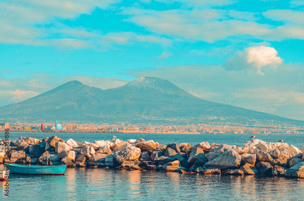 Fototapeta premium view of Mount Vesuvius and the Gulf of Naples with rocks and blue boat. Naples, Italy