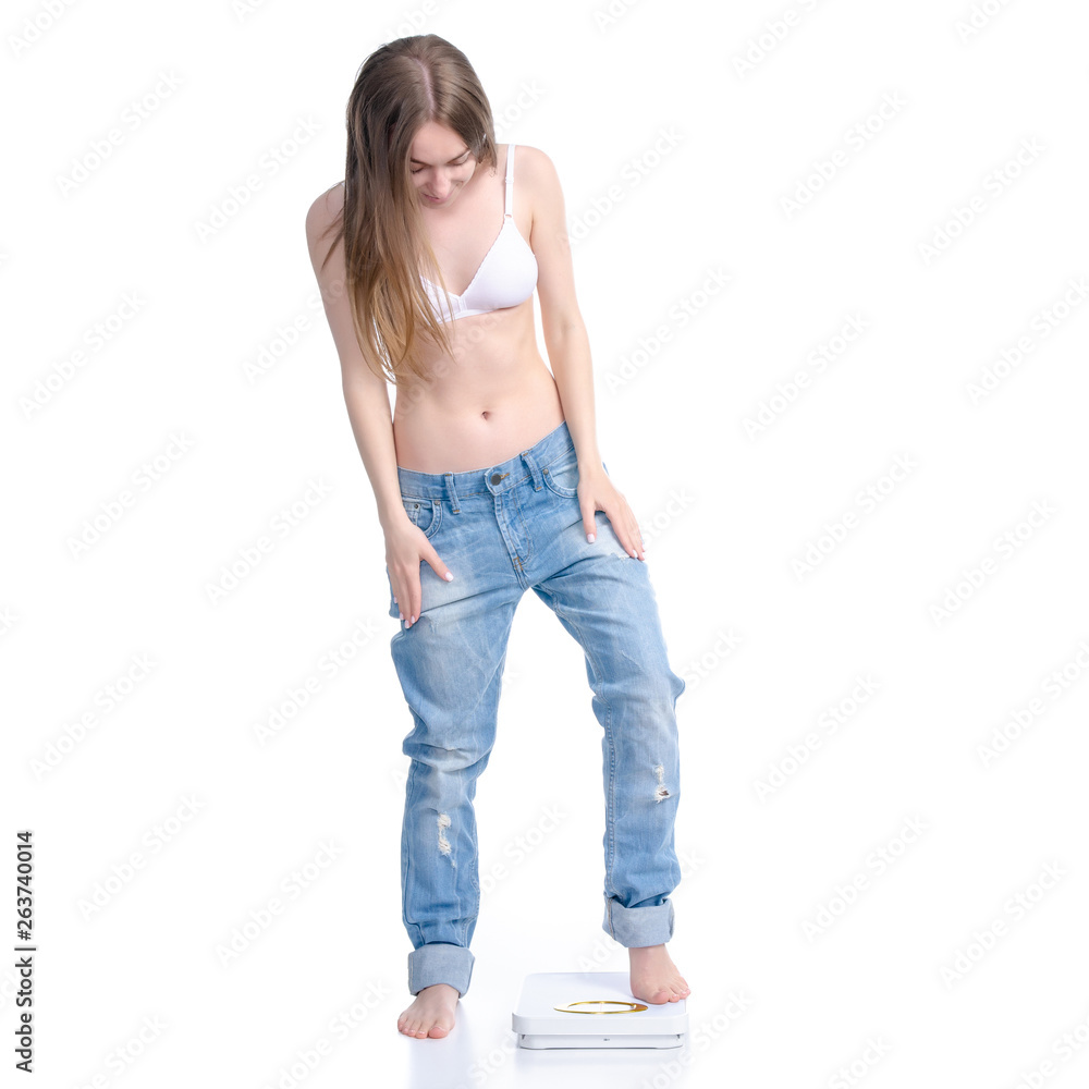 Beautiful woman in big jeans on weighing-machine, weight loss slimming on a white background. Isolation Beautiful woman in big jeans on weighing-machine, weight loss slimming on a white background. Isolation