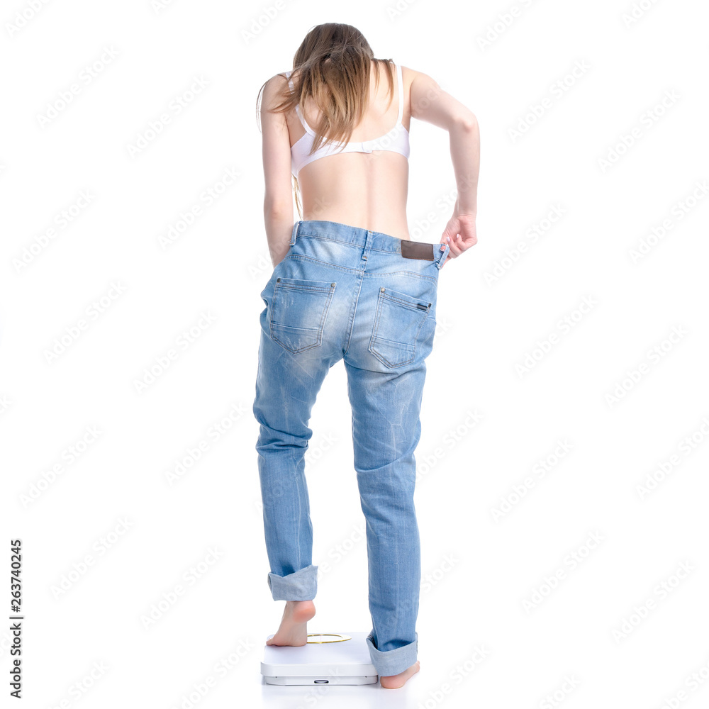 Beautiful woman in big jeans on weighing-machine, weight loss slimming on a white background. Isolation, back-view Beautiful woman in big jeans on weighing-machine, weight loss slimming on a white background. Isolation, back-view