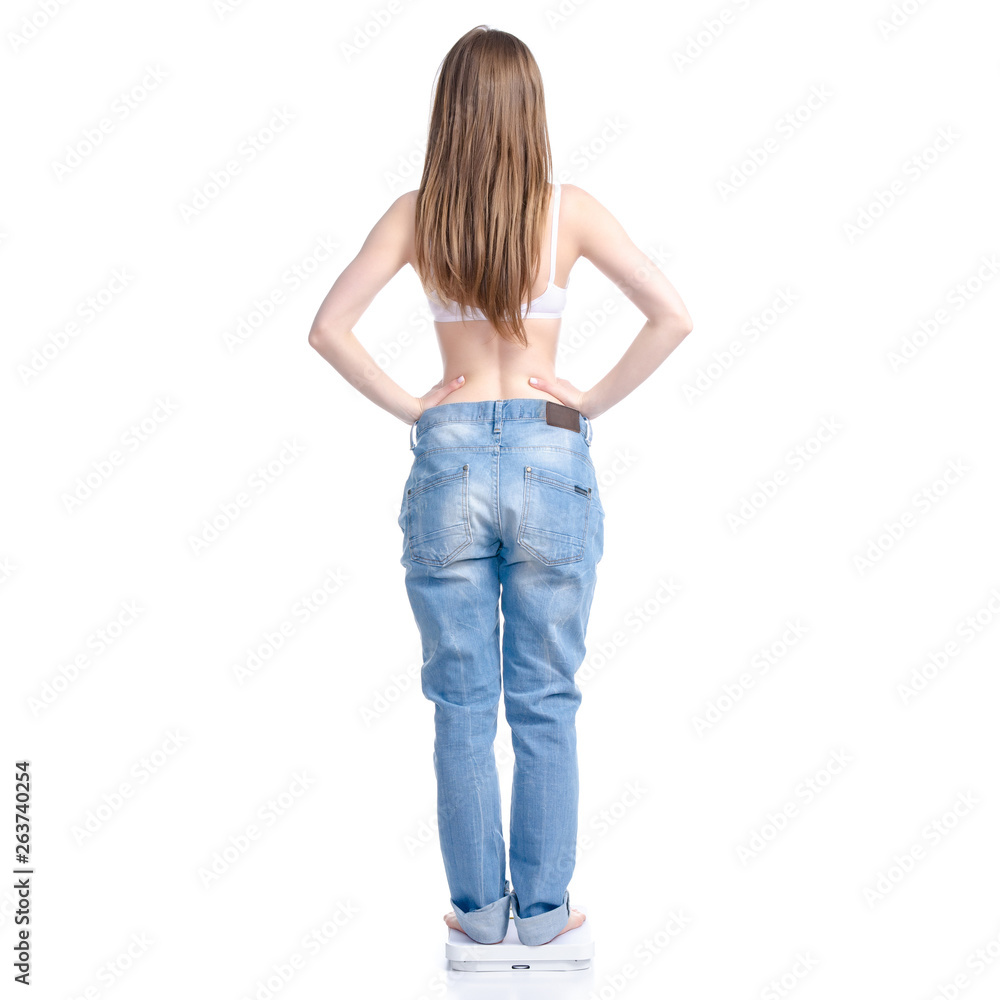 Beautiful woman in big jeans on weighing-machine, weight loss slimming on a white background. Isolation, back-view Beautiful woman in big jeans on weighing-machine, weight loss slimming on a white background. Isolation, back-view