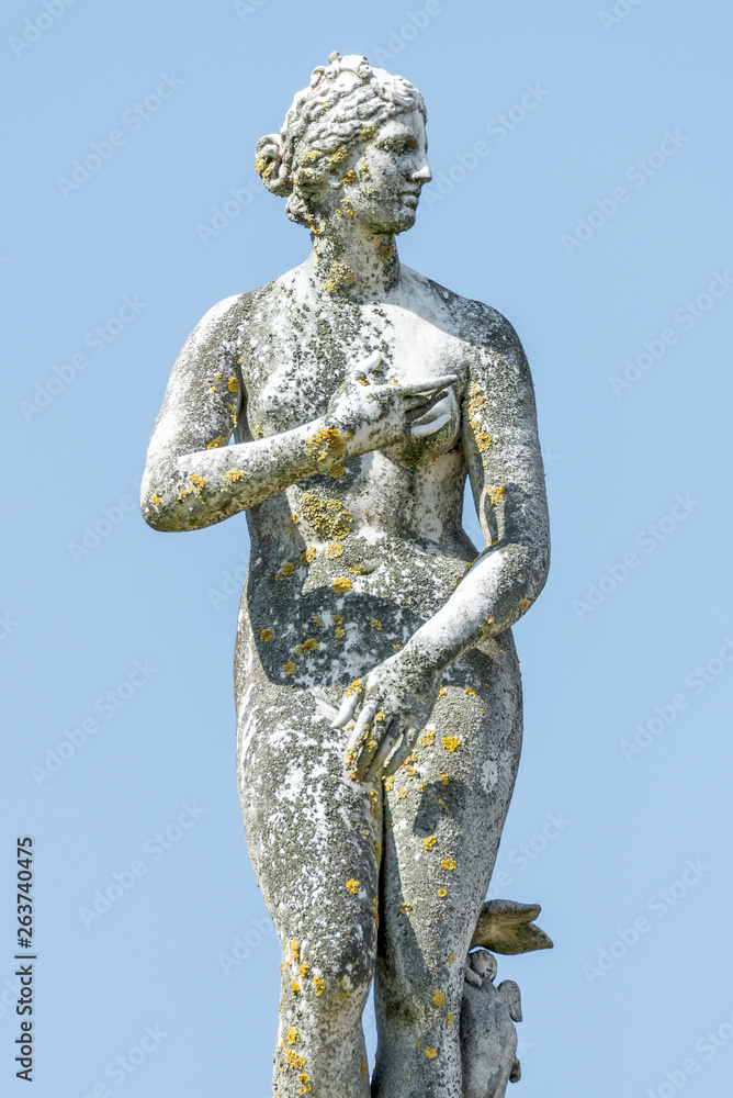 Ancient statue covered with moss and lichen of a sensual renaissance era woman in Potsdam, Germany