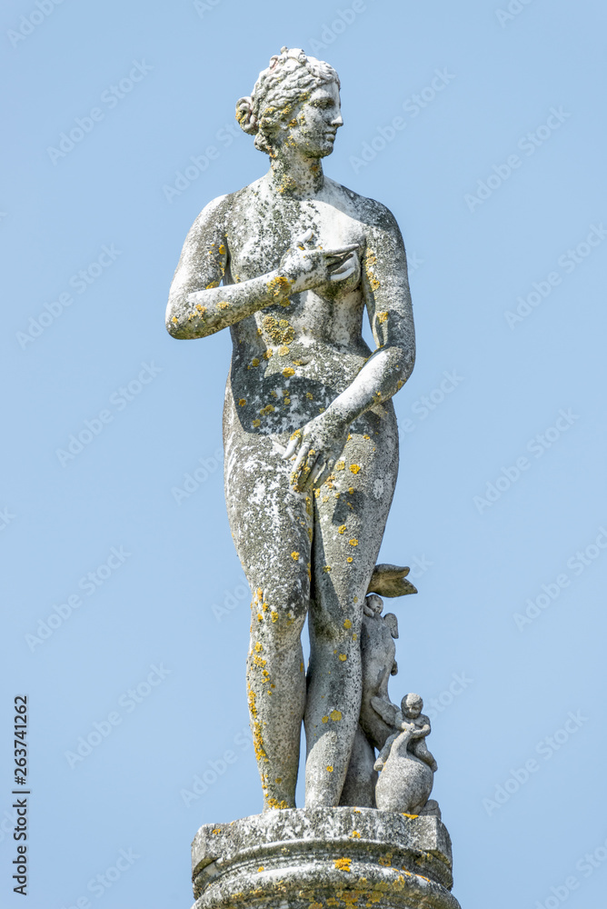 Ancient statue covered with moss and lichen of a sensual renaissance era woman in Potsdam, Germany