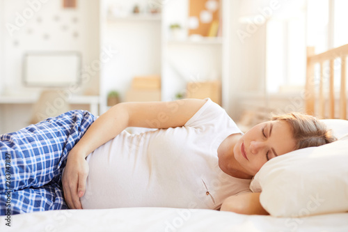 Portrait of pregnant woman sleeping in comfortable bed hugging belly, copy space
