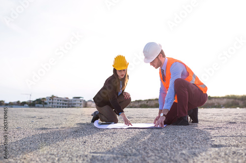 Ingegneri uomo e donna inginocchio sulla spiaggia di fronte a un progetto per la costruzione nel cantiere. photo
