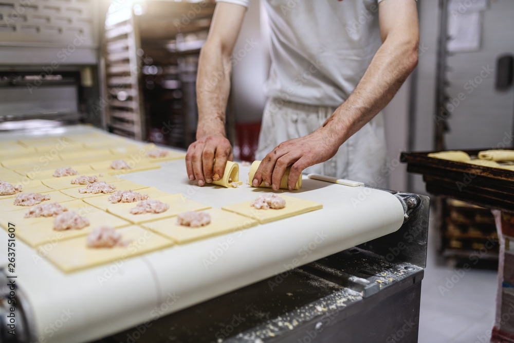 Fototapeta premium Caucasian baker dressed in clean white uniform making sweet puff pastry while standing in bakehouse.