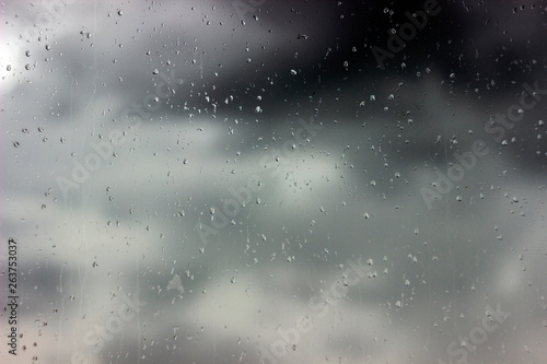 raindrops on glass in cloudy weather on gray background © Yekatseryna