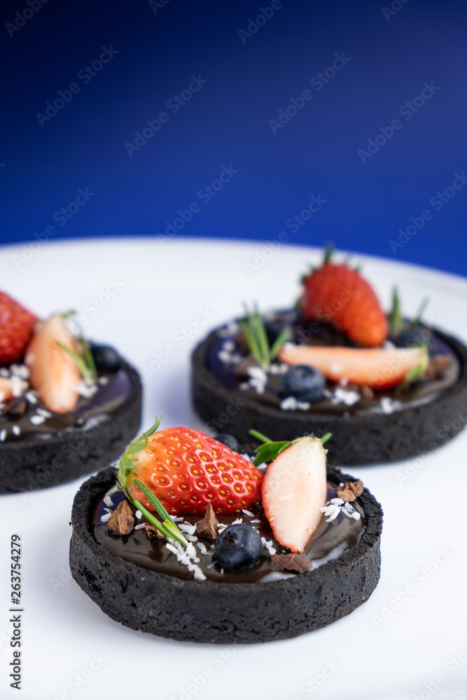 Cookie crust chocolate tart with Blueberry and strawberry set on Blue Background.