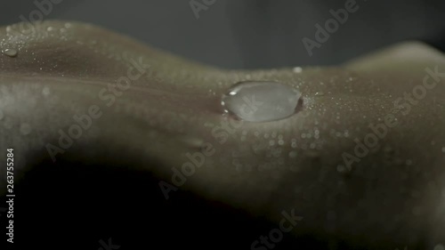 Macro close-up of a melting ice cube slowly sliding into the bare belly button of a sexy toned woman's stomach