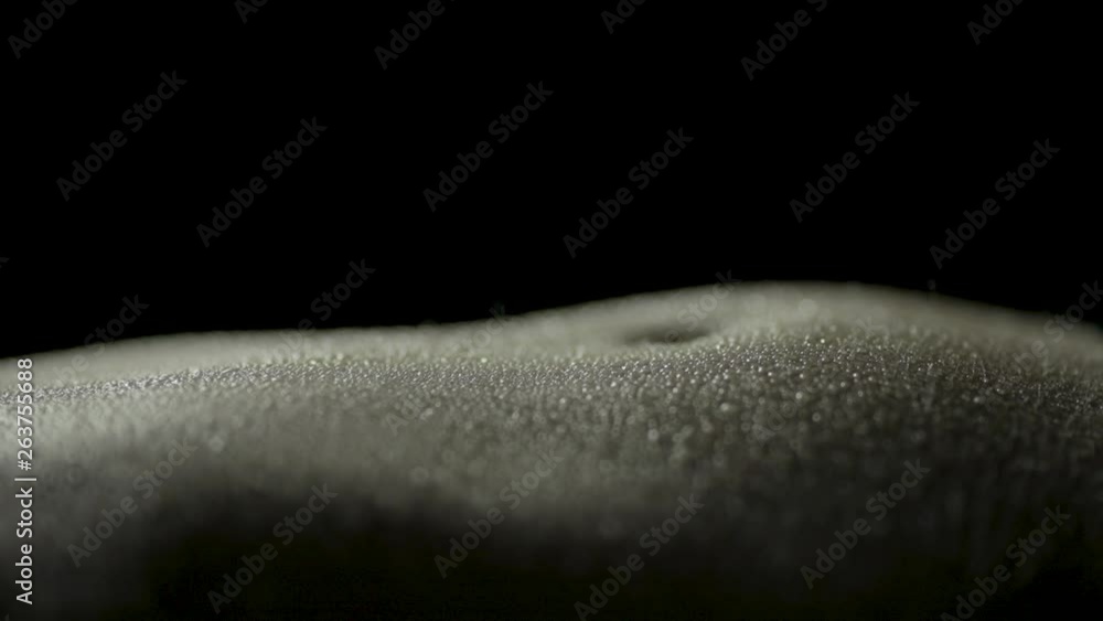 Macro close-up of a woman's wet, glistening stomach while breathing as she is laying down with a black background Macro close-up of a woman's wet, glistening stomach while breathing as she is laying down with a black background