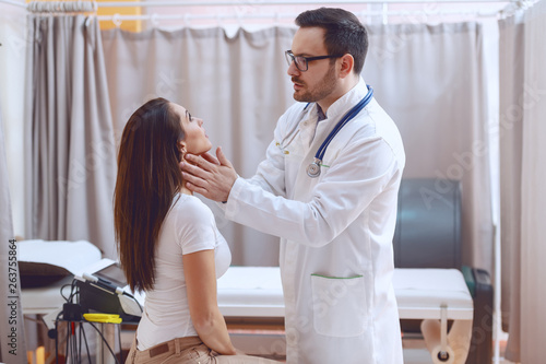 Young Caucasian doctor in white uniform examining patient s throat while standing at hospital.