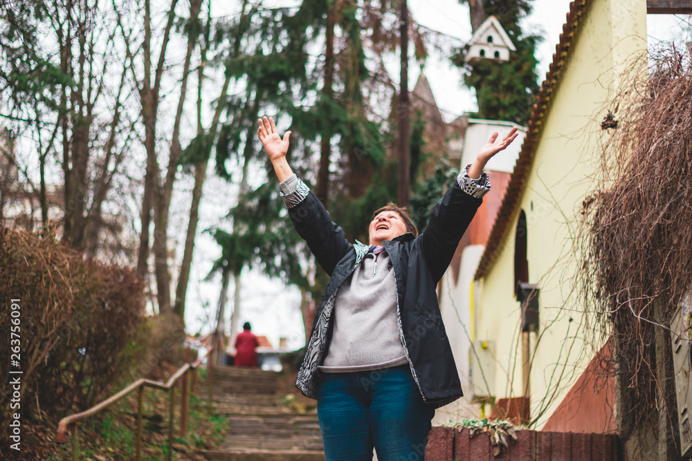 Happy old woman expressing joy with her arms straight up in the air outside – Smiling beautiful grandmother holding her arms up standing on stairs showing enthusiasm