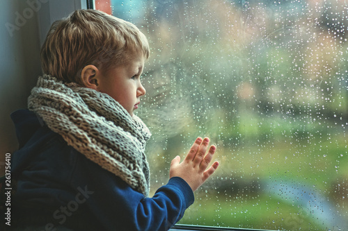 Boy dressed in a warm scarf near the window with raindrops