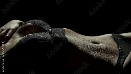 Close-up of a woman's sensual and wet body lying down in black lingerie as she runs her hand down her body