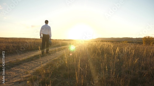 businessman in sunglasses goes down the country road with a briefcase in his hand. The entrepreneur works in a rural area. a farmer inspects land at sunset. agricultural business concept.