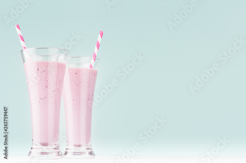 Two blueberry milk cocktails in elegant glass with straws in soft light mint green interior, copy space.