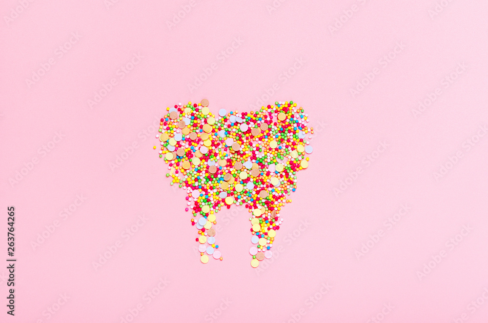 Tooth from confectionery dressing on a pink background. The concept of harmful sweets, dental health and smiles. Top view, flat lay.