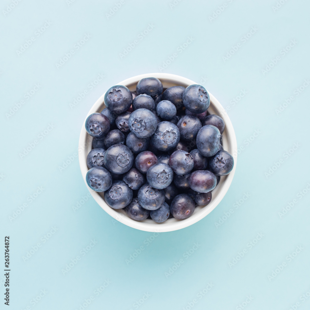 Fresh ripe blueberries in white bowl on a blue bright background Fresh ripe blueberries in white bowl on a blue bright background