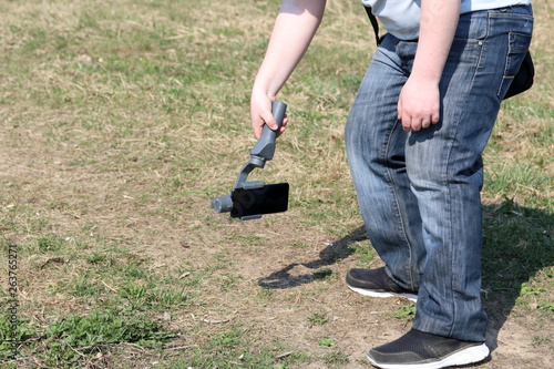 A young man videotaping on a smartphone. Uses gimbal to get smooth shots. Keeps record low on the ground.