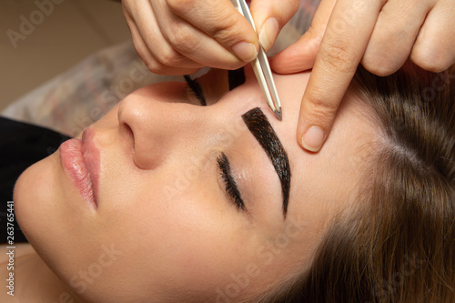 Young woman having professional eyebrow correction procedure in beauty salon
