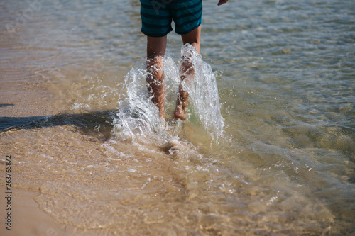 Back view of man bare foot walking on the summer beach. Close up leg of man walking in the sea, splash around