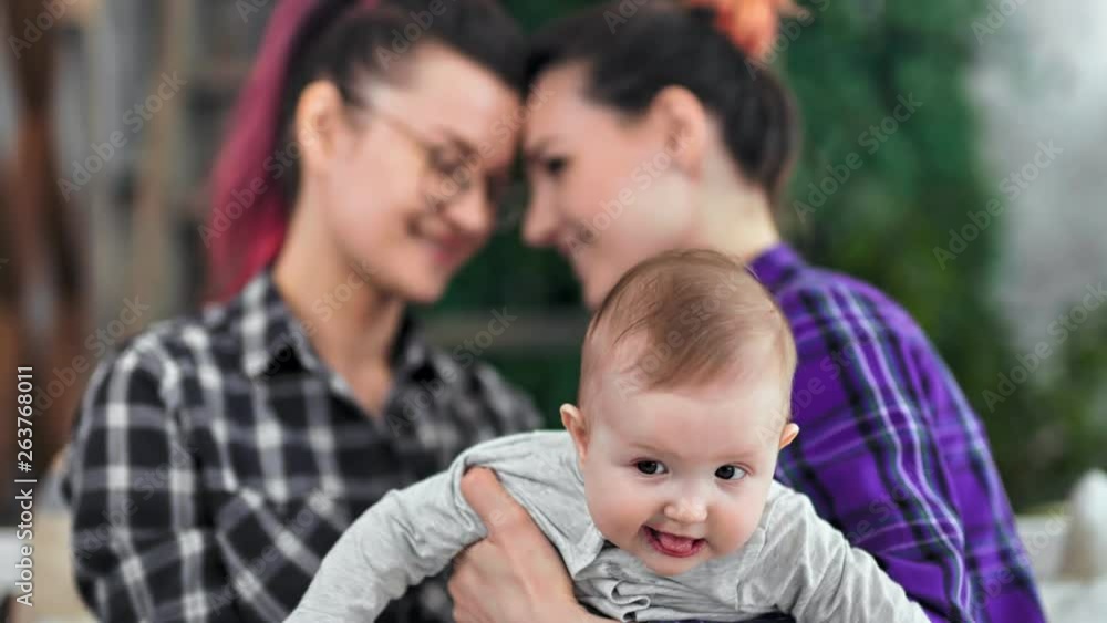 Close-up little cute baby holding by hand of same sex couple having good time together at home Close-up little cute baby holding by hand of same sex couple having good time together at home