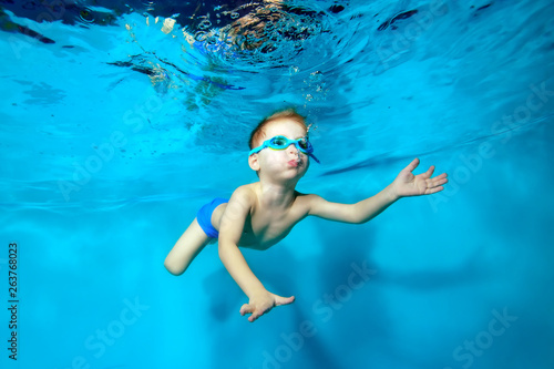Happy little boy swimming underwater in the pool and blowing bubbles on blue background. Portrait. Underwater photography. Horizontal orientation