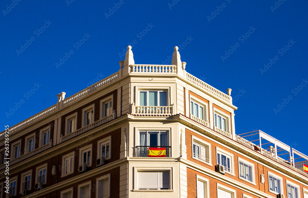 Spanish residential building facade with Spanish flag in the window and blue cloudless sky above in Madrid, Spain. Architecture. Sunny day.
