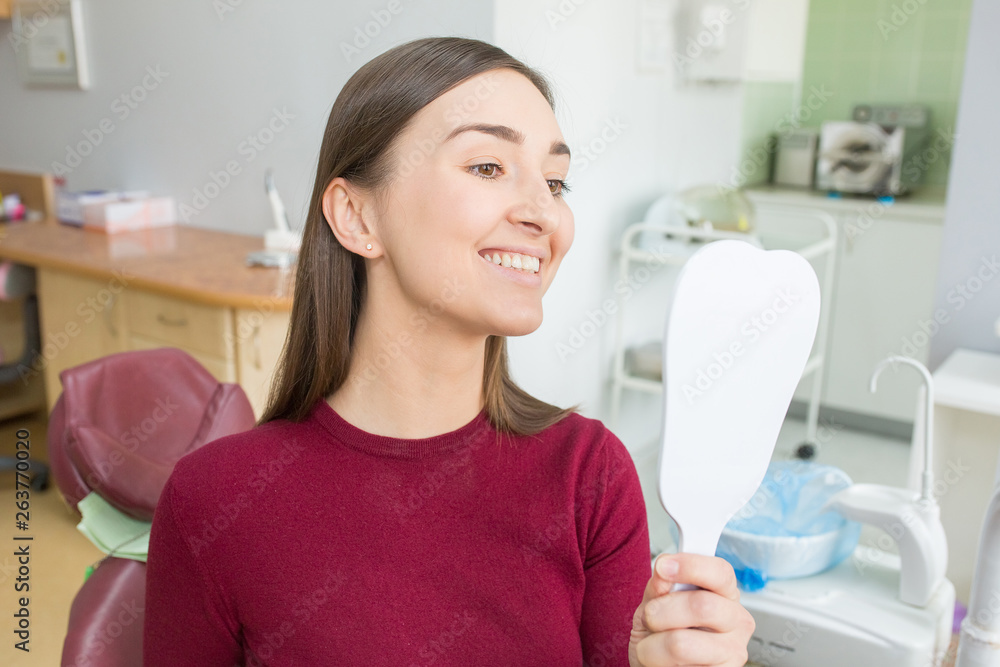Young woman sits in a dental chair looking in mirror as a patient. People health care, dentistry, medicine concept. Doctor and patient. Teeth dentist with patient in hospital Young woman sits in a dental chair looking in mirror as a patient. People health care, dentistry, medicine concept. Doctor and patient. Teeth dentist with patient in hospital