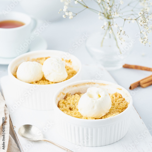 Close up apple crumble with ice cream, spoon with streusel. Side view, vertical. Morning breakfast on a light gray table.