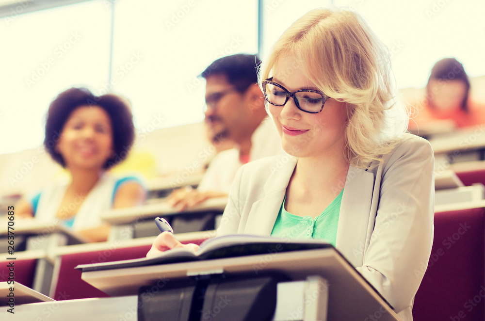 education, high school, university, learning and people concept - student girl writing to notebook in lecture hall education, high school, university, learning and people concept - student girl writing to notebook in lecture hall