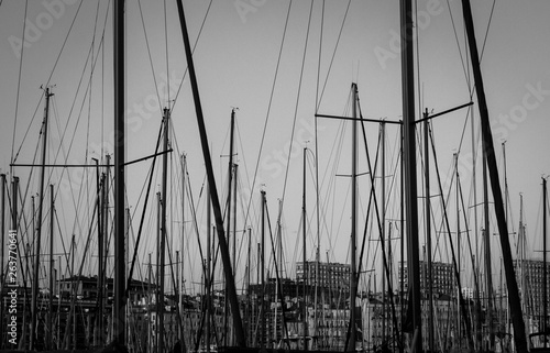 Yacht masts and various yachts on the foreground and city center on the background in Marseille bay. Evening time. Provence, France. Black and white photo. Marine view.