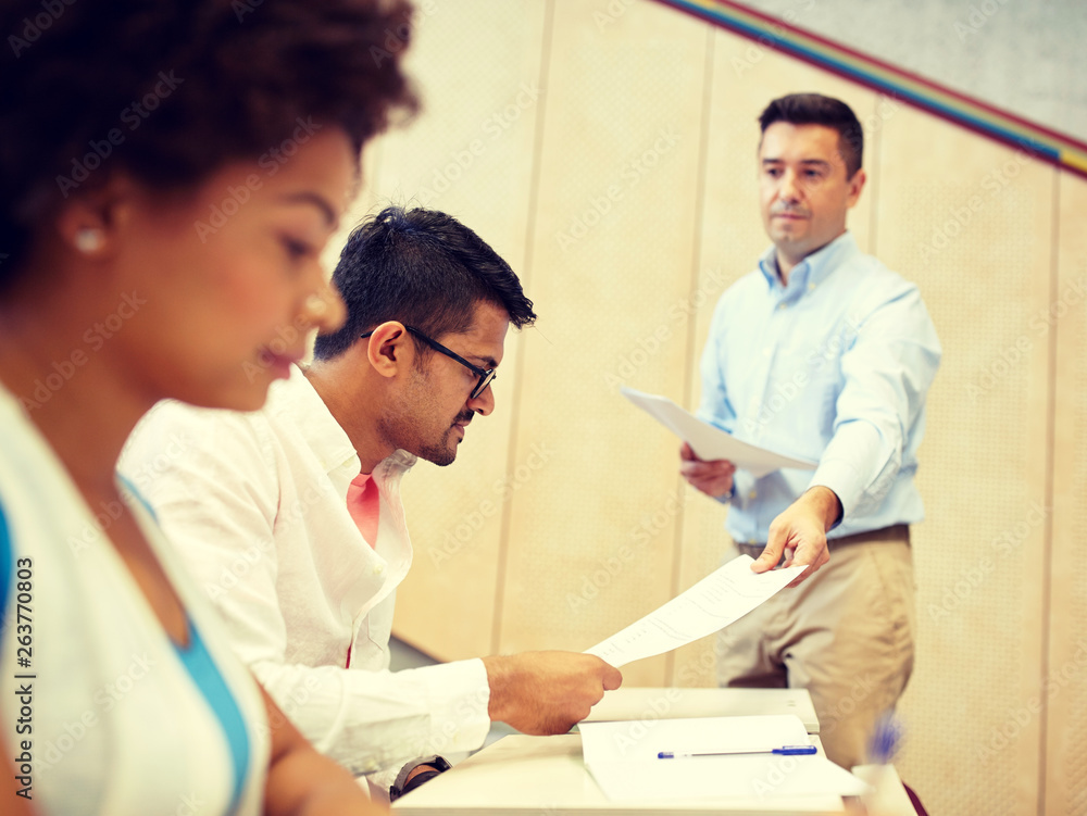 Obraz premium education, high school, university, learning and people concept - teacher giving tests to students at lecture