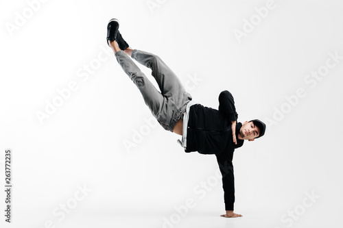 Stylish young man is dancing breakdance. He is standing on one arm and lifting both legs up.
