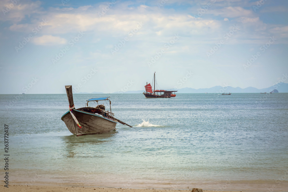 Thai longtail boat on the beach of Phra Nang. Going to the sea, on background of a black sailing ship with red sails