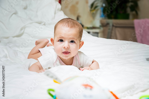 Increased salivation in the infant during teething. A baby girl in white clothes is lying on a white bed, smiling, drooling. Salivary glands activation