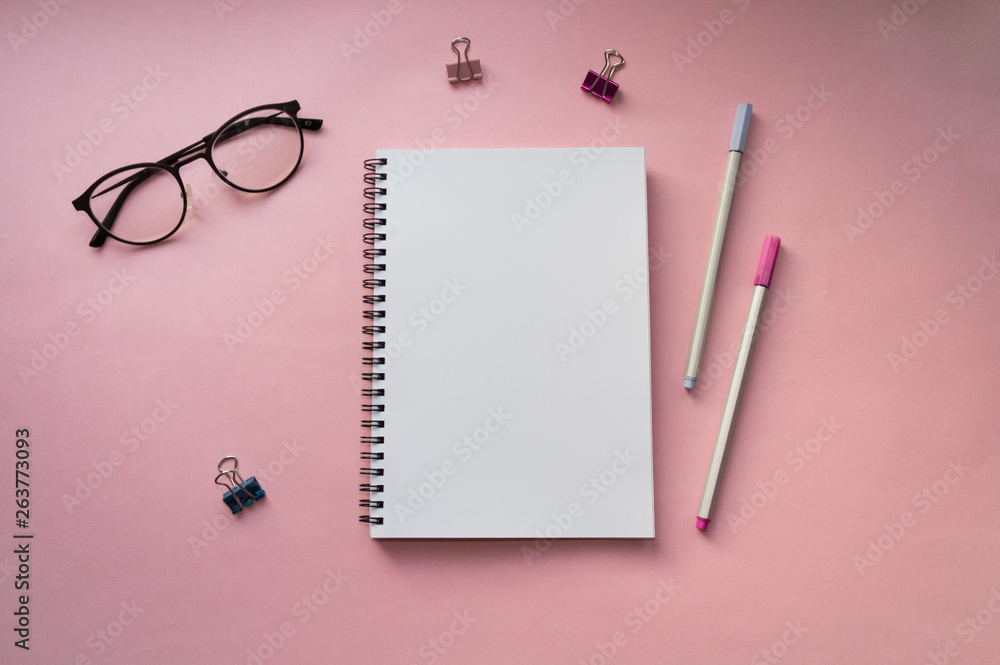 Empty white notebook top view on pink background close to pen, clips and glasses Empty white notebook top view on pink background close to pen, clips and glasses