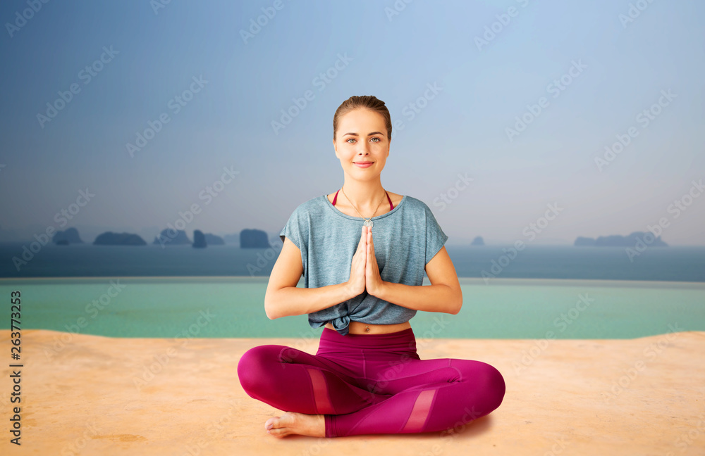 Fototapeta premium mindfulness, spirituality and healthy lifestyle concept - woman doing outdoor yoga and meditating in lotus pose over infinity edge pool background