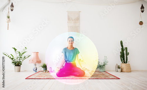 mindfulness, spirituality and healthy lifestyle concept - woman meditating in lotus pose at yoga studio over rainbow aura photo