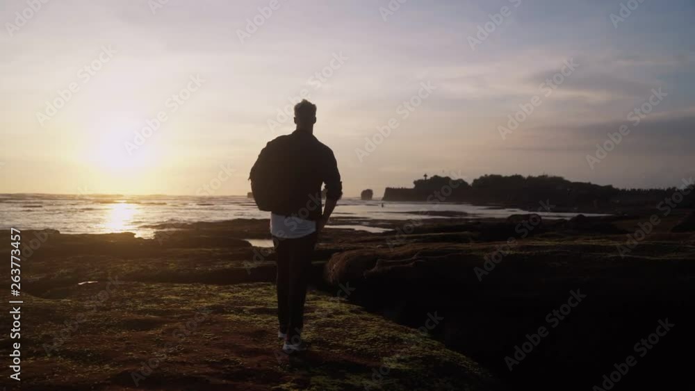 Young man walks along beach, jumps, opens his arms wide against beautiful sunset. Slow motion Young man walks along beach, jumps, opens his arms wide against beautiful sunset. Slow motion