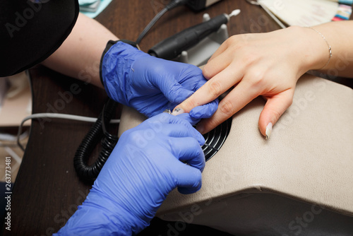 Closeup shot of a woman in a nail salon receiving a manicure by a beautician with electric nail file. Woman getting nail manicure. Beautician file nails to a customer